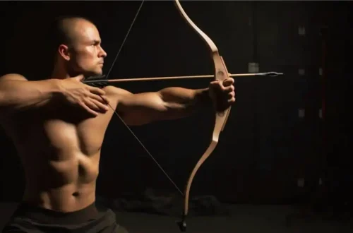 shirtless man holds a bow and arrow while training in archery