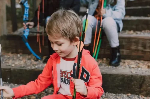 a young boy wearing a red hoodie holds onto some arrows outdoors
