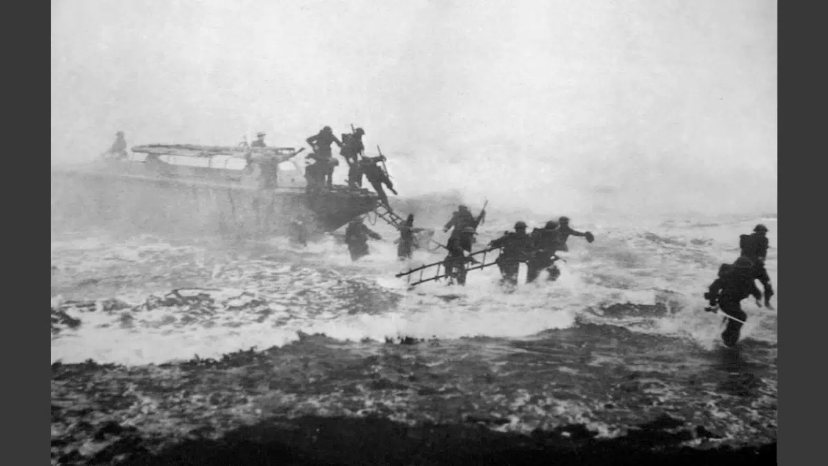 a black and white image during World War II of soldiers jumping off a boat onto the shore carrying their rifles, leading the soldiers on the right is a soldier carrying a sword