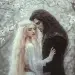 a beautiful river nymph wearing a long white gown with blond white hair embraces a yound Hades, with long dark hair wearing dark clothes in a forest of white leaved trees