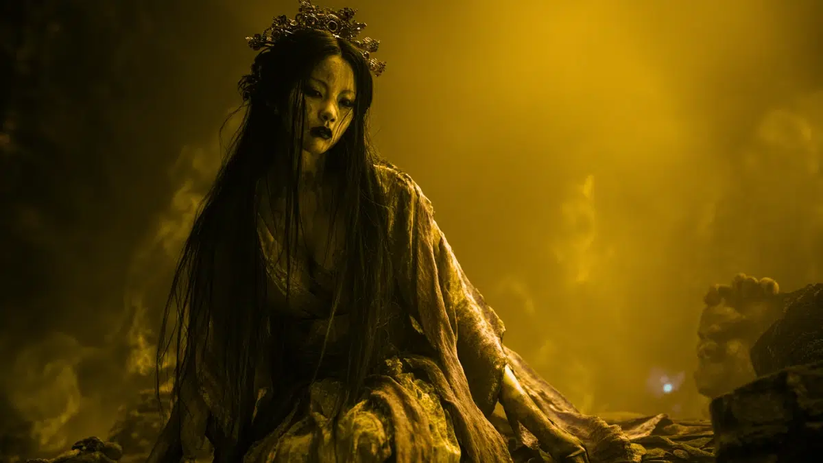 Izanami as queen of Yomi, illuminated by dim orange underworld glow, long dark hair cascading around her, traditional robes